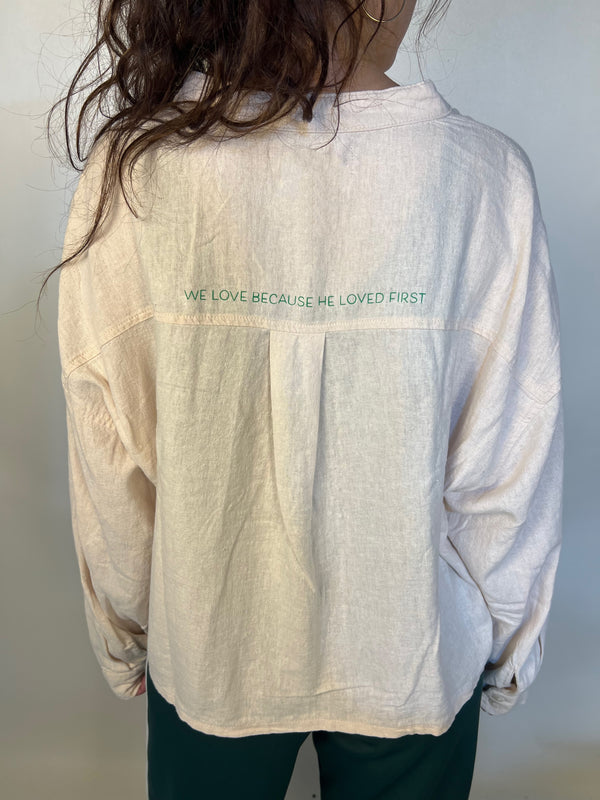 Girl in tailored cactus beige button up with ‘we love because he loved first’ on back