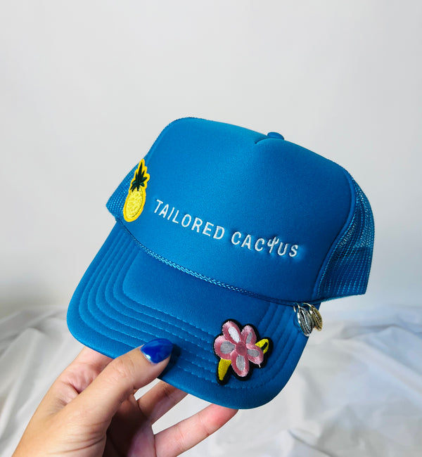 Tailored cactus blue trucker hat with seashell charms and flower patches 