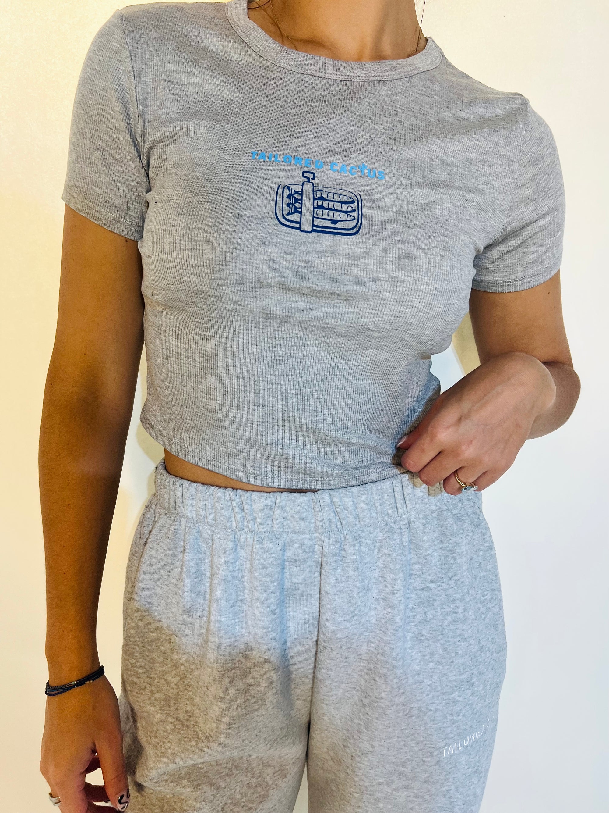 Person wearing a gray t-shirt with a logo and matching gray sweatpants on a plain background