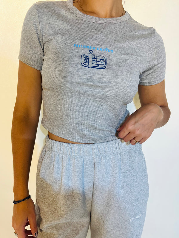 Person wearing a gray t-shirt with a logo and matching gray sweatpants on a plain background