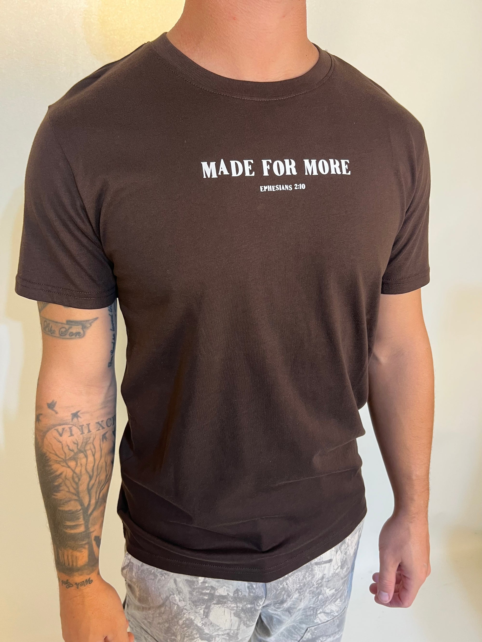 Person wearing a brown t-shirt with 'MADE FOR MORE' text on a plain background