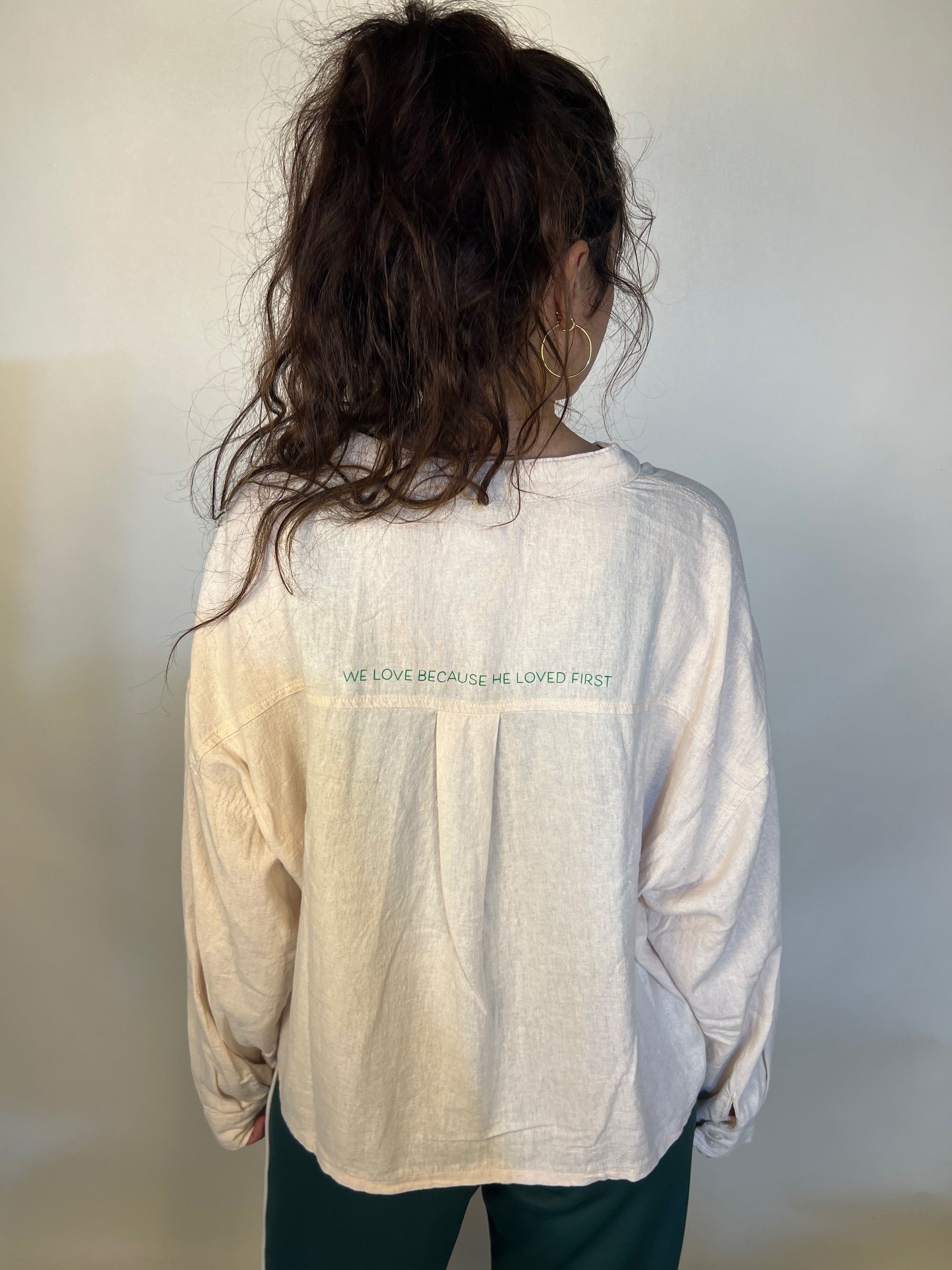 Girl in tailored cactus beige button up with ‘we love because he loved first’ on back 