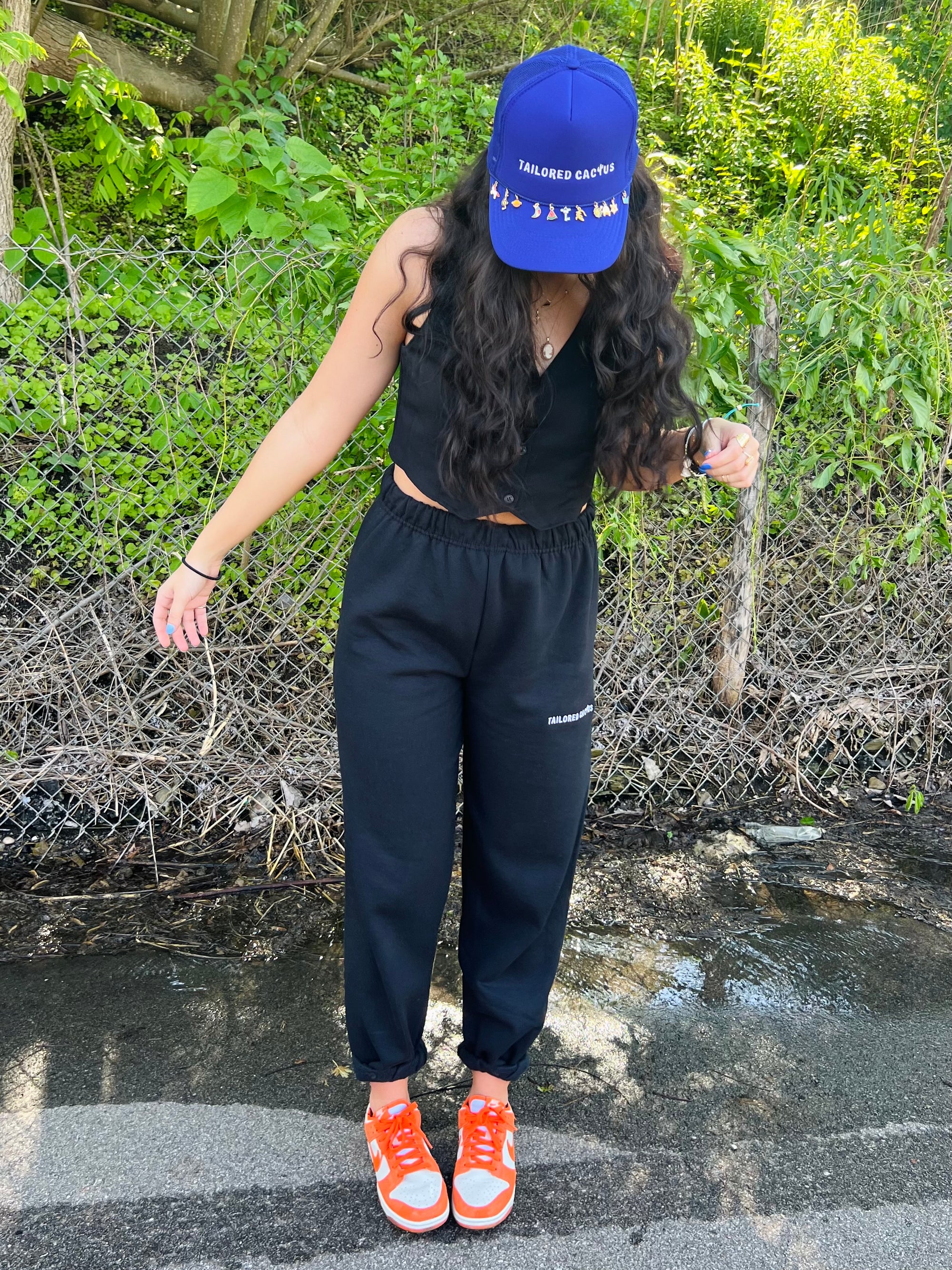 Tailored cactus girl in purple charm trucker hat and black sweatpants 