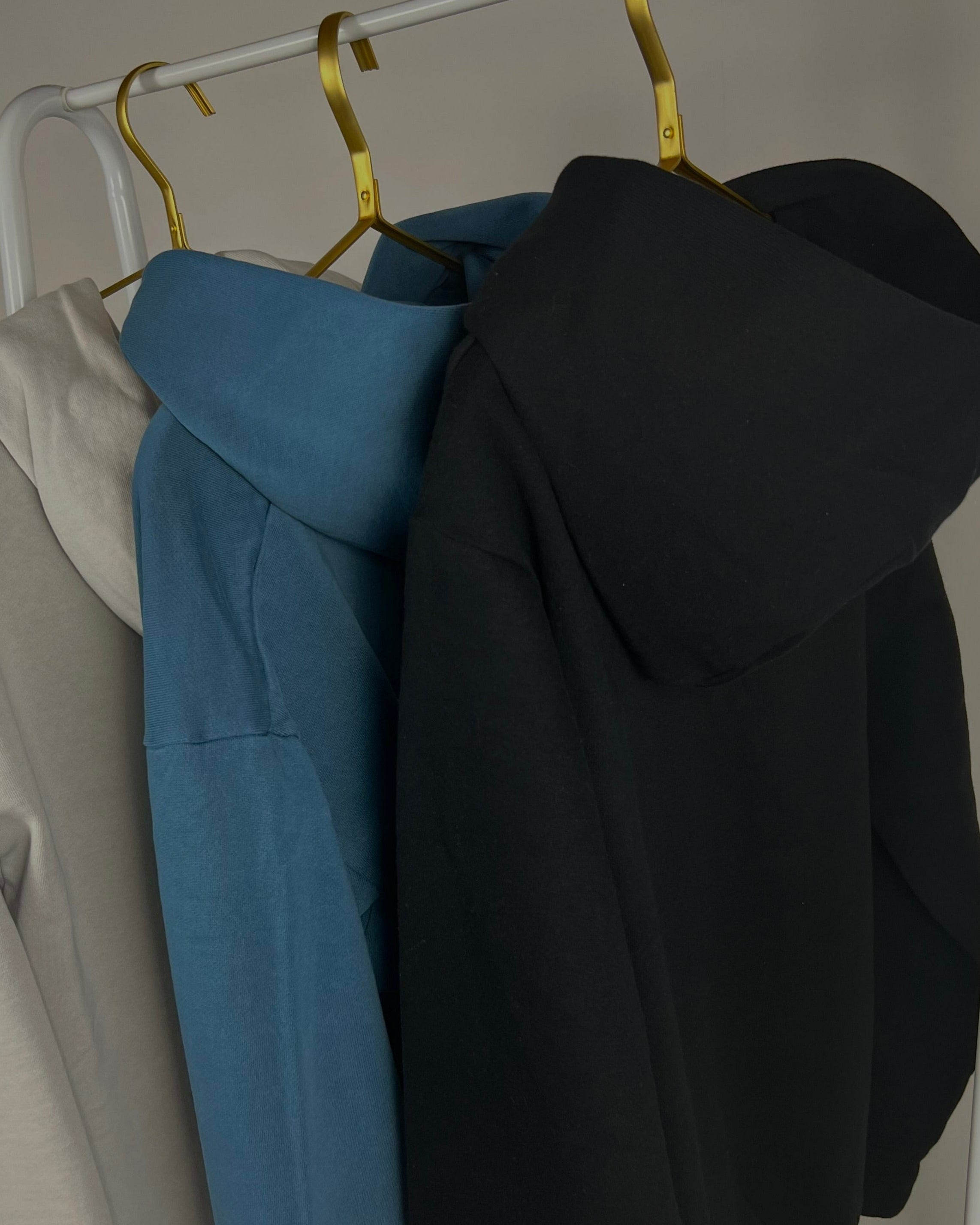 tailored cactus hoodies hanging up in black,  blue, and white