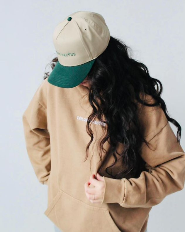 Tailored Cactus female model wearing tan hoodie and tan and green trucker hat